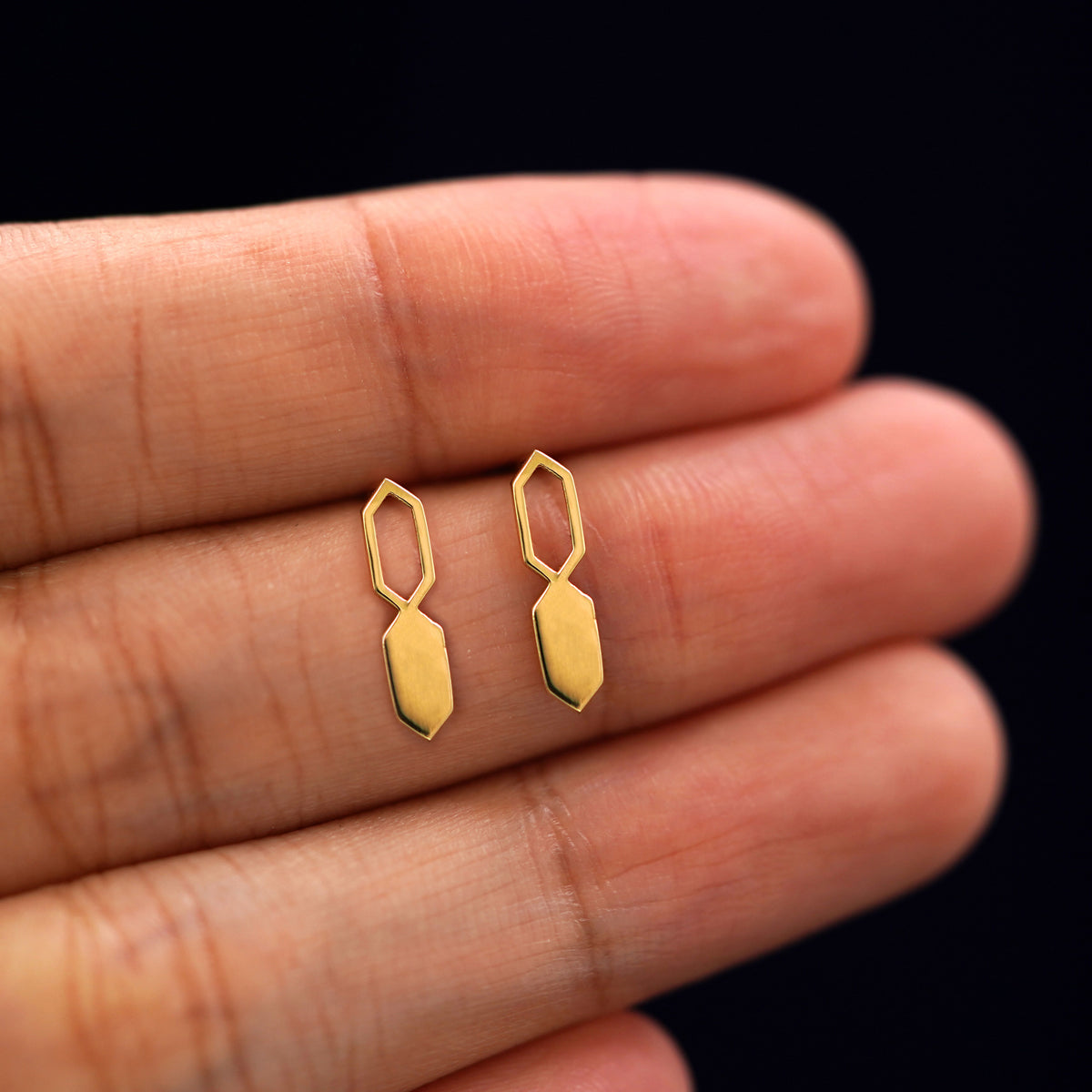 A model's hand holding a pair of recycled 14k gold Tanlah Earrings