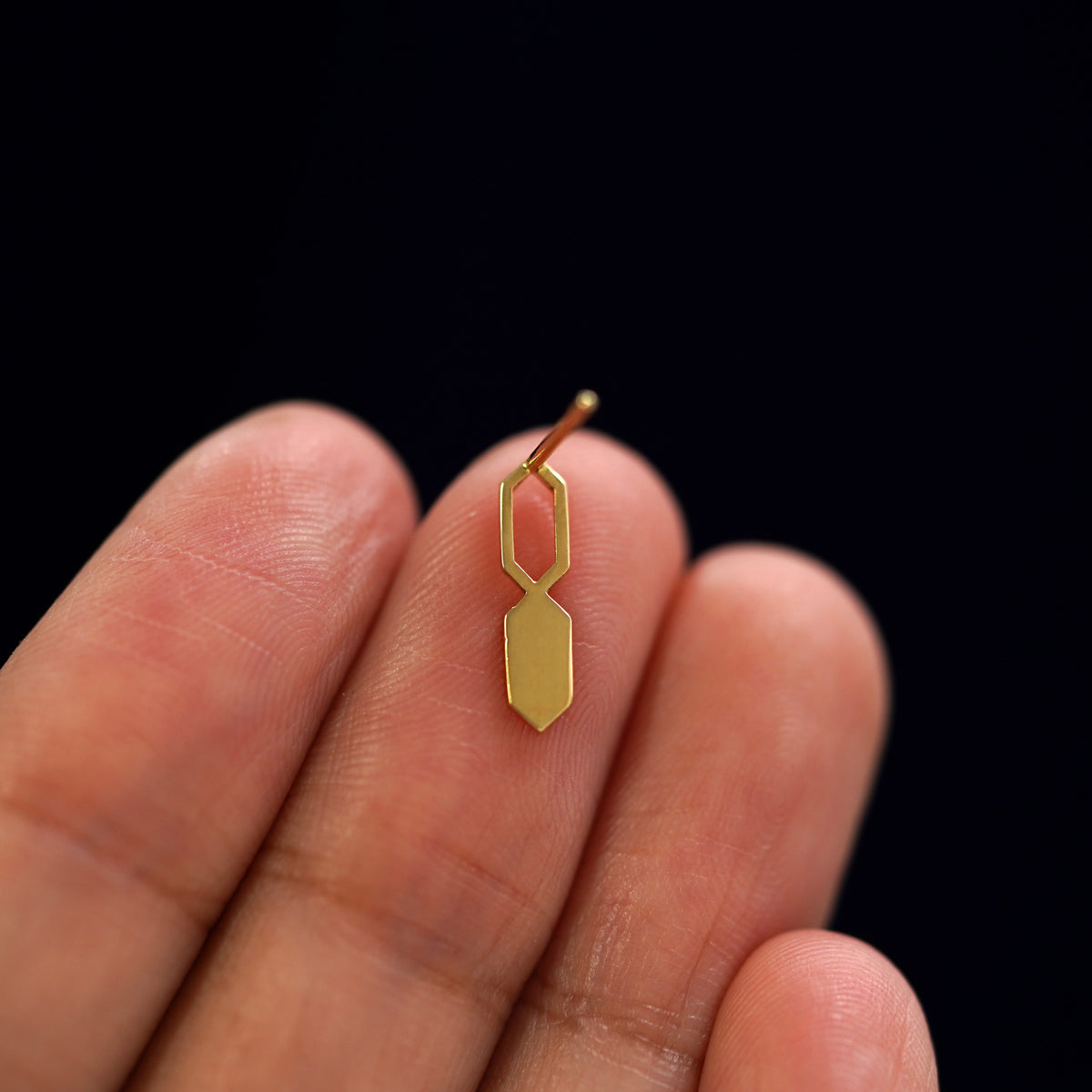 A yellow gold Tanlah Earring laying facedown on a model's fingers to show the underside view