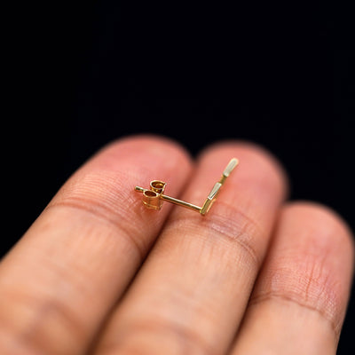 A 14k gold Tanlah Earring sitting sideways on a model's fingertips to show detail