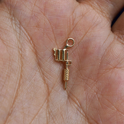 A 14k gold Tattoo Machine Charm for earring resting in a model's palm to show the underside of the charm