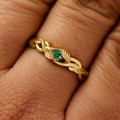 A solid 14k yellow gold teal sapphire leaves and vines ring on a model's finger