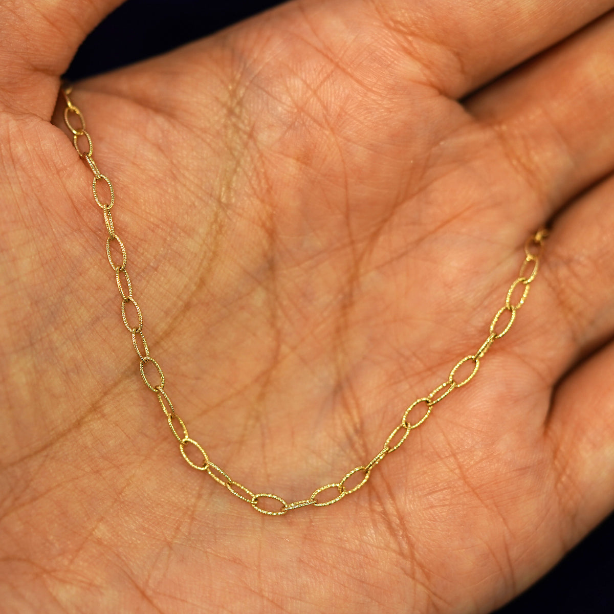 A yellow gold Veren Anklet draped on a model's palm