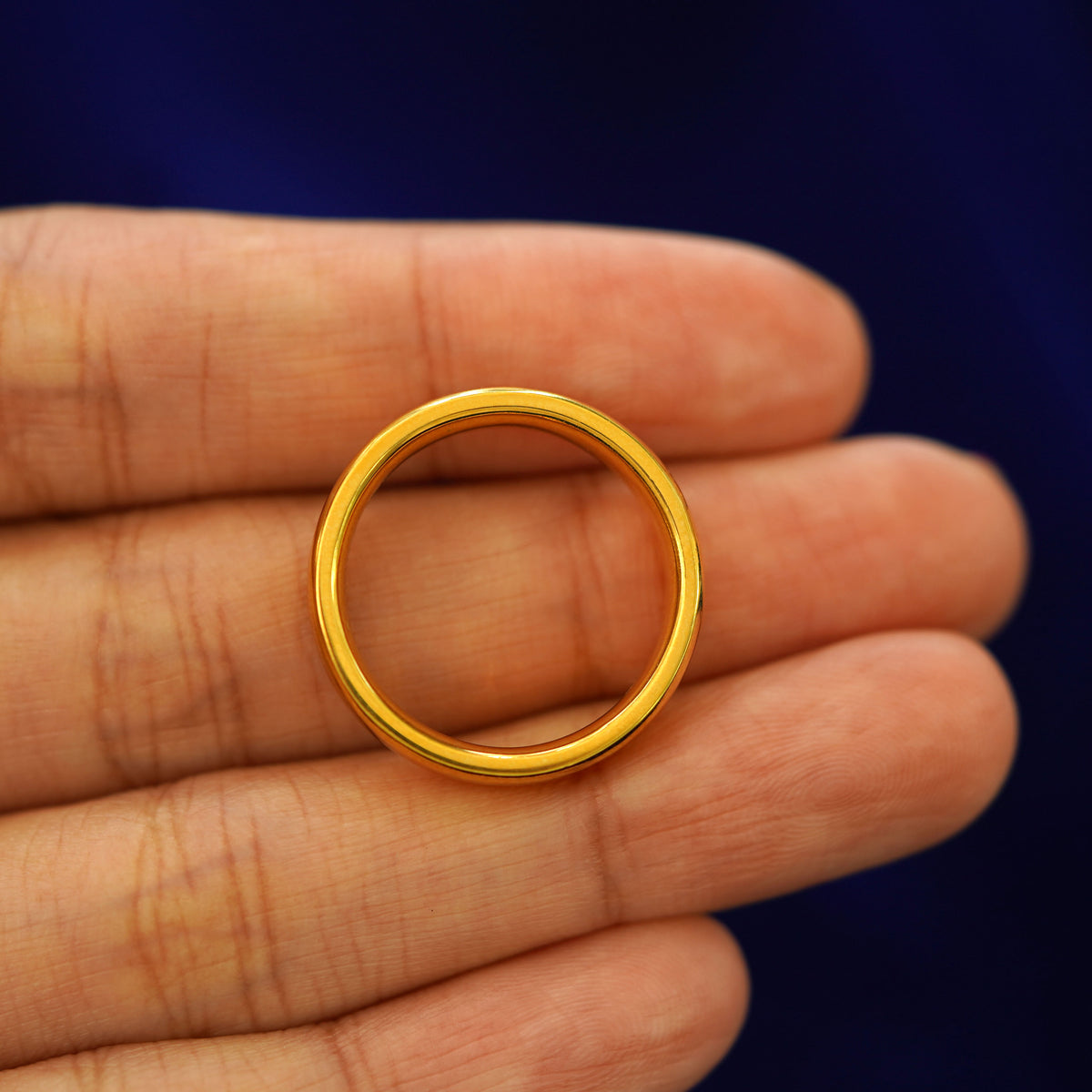 A yellow gold 24k Mix Mirror Band in a model's hand showing the thickness of the band