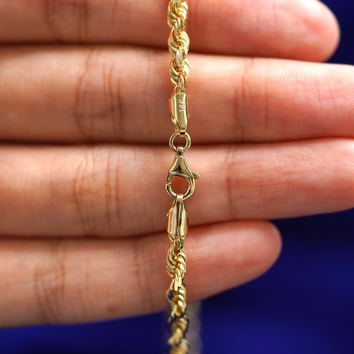 A lobster claw clasp on a 14k yellow gold Thick Rope Bracelet laying across a model's fingers