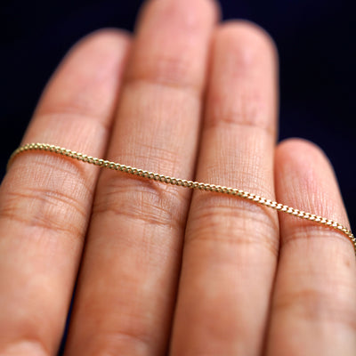 A yellow gold Mini Miami Anklet resting on a model's fingers