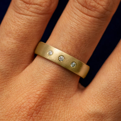Close up view of a model's fingers wearing a 14k yellow gold Mix Matte Band with three diamonds