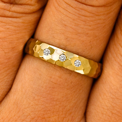 Close up view of a model's fingers wearing a 14k yellow gold Curvy Hammered Band with 3 diamonds