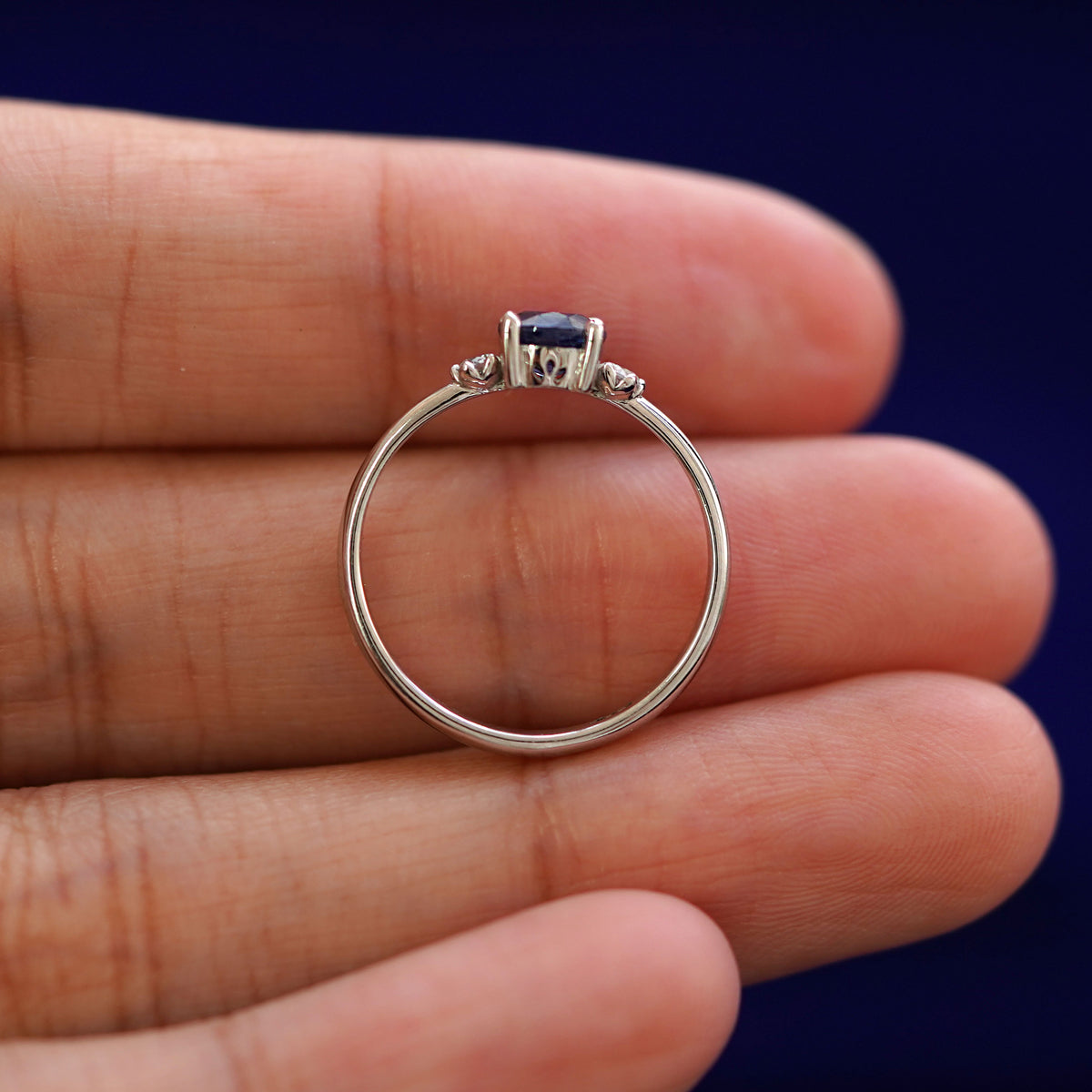A white gold Three Stone Sapphire Ring in a model's hand showing the thickness of the band
