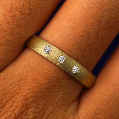 Close up view of a model's fingers wearing a 14k yellow gold Curvy Stardust Band with three gems