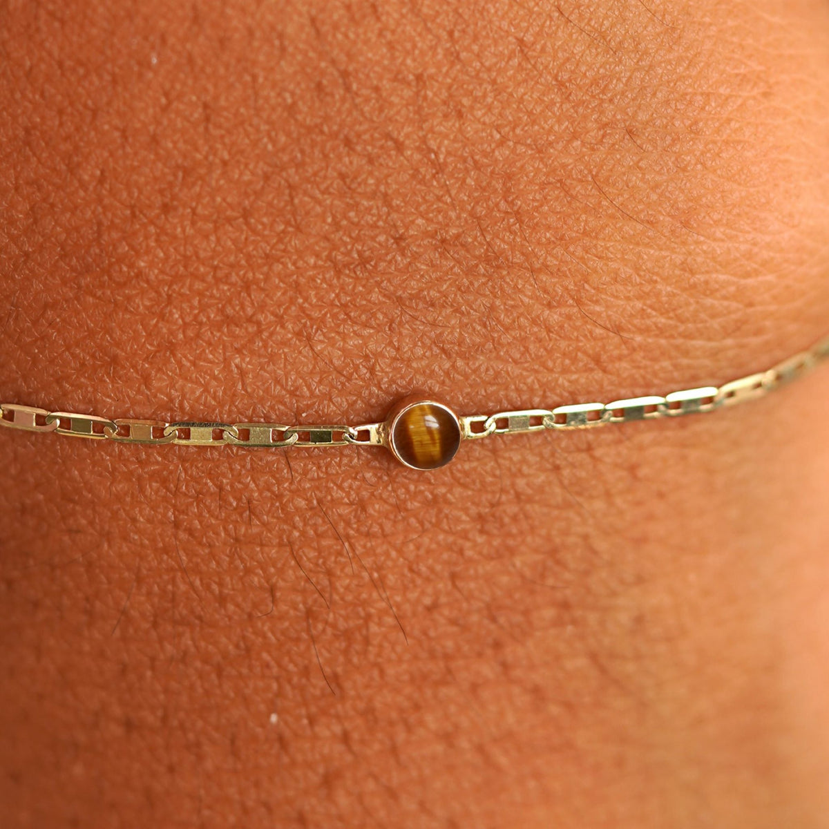 Close up view of a models wrist wearing 14k yellow gold Tiger Eye Bracelet