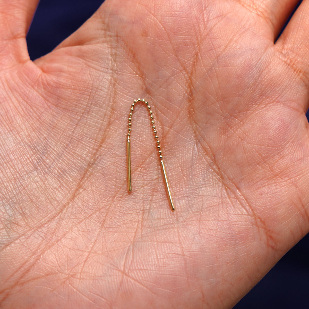 A solid 14k yellow gold Mini Threader sitting in a model's palm with the beaded chain in a arch to show its flexibility