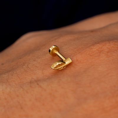 A solid 14k yellow gold Mini Leaf Flatback Piercing resting on the back of a model's hand