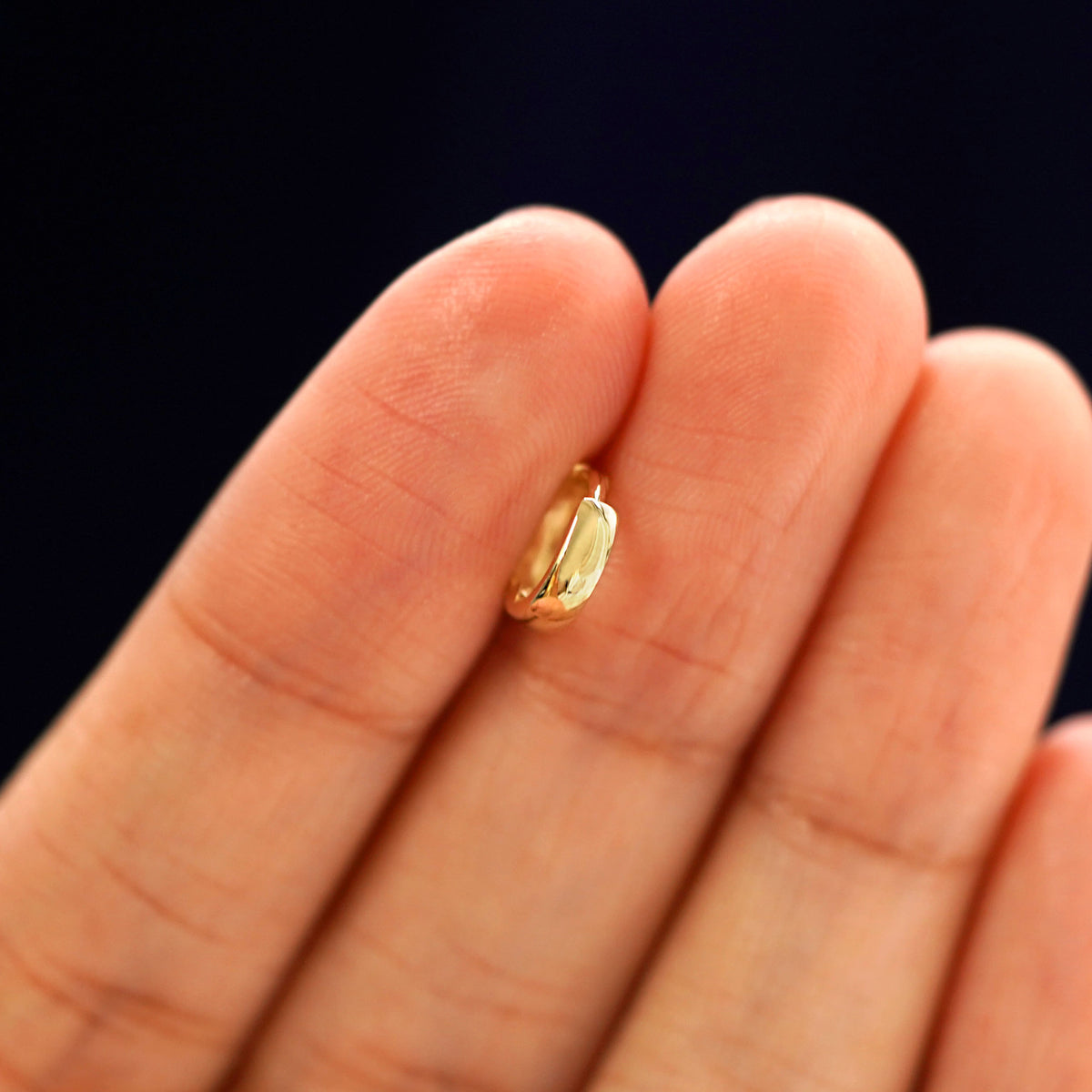 A 14k gold Mini Thick Huggie Hoop Earring held in between a model's fingers to show the hoops thickness