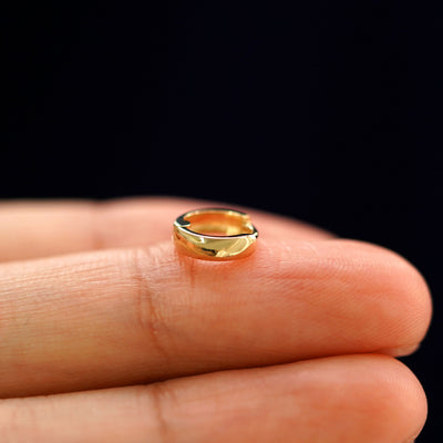 A yellow gold Mini Thick Huggie Hoop Earring laying sideways on a model's fingertips