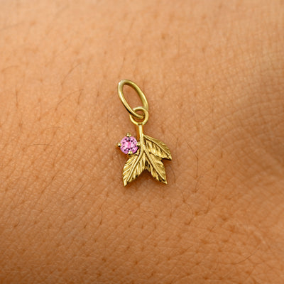 A solid 14k yellow gold pink tourmaline Gemstone 3 Leaves Charm resting on the back of a model's hand