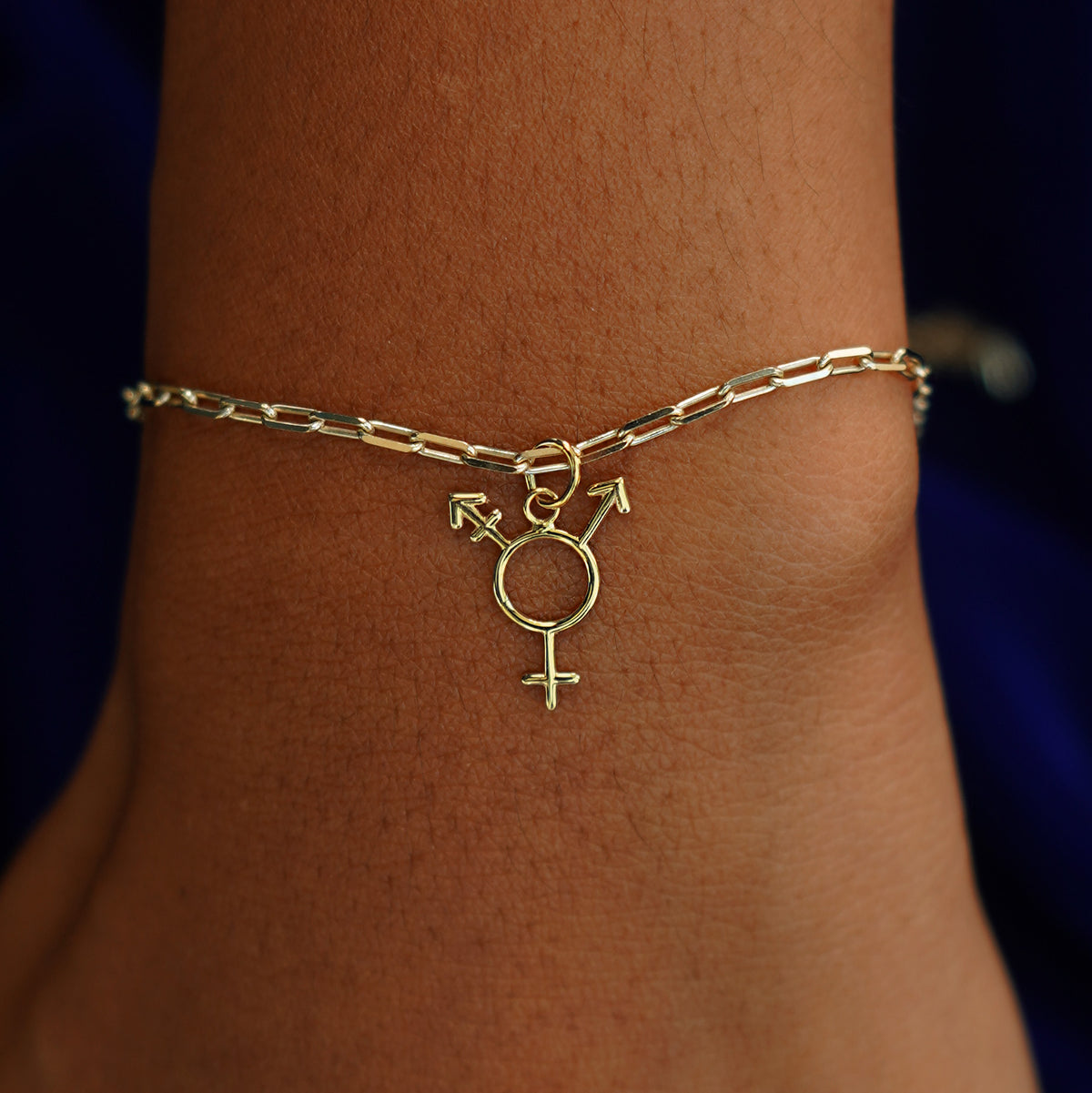 A model's wrist wearing a yellow gold Trans Symbol Charm on a Butch Bracelet