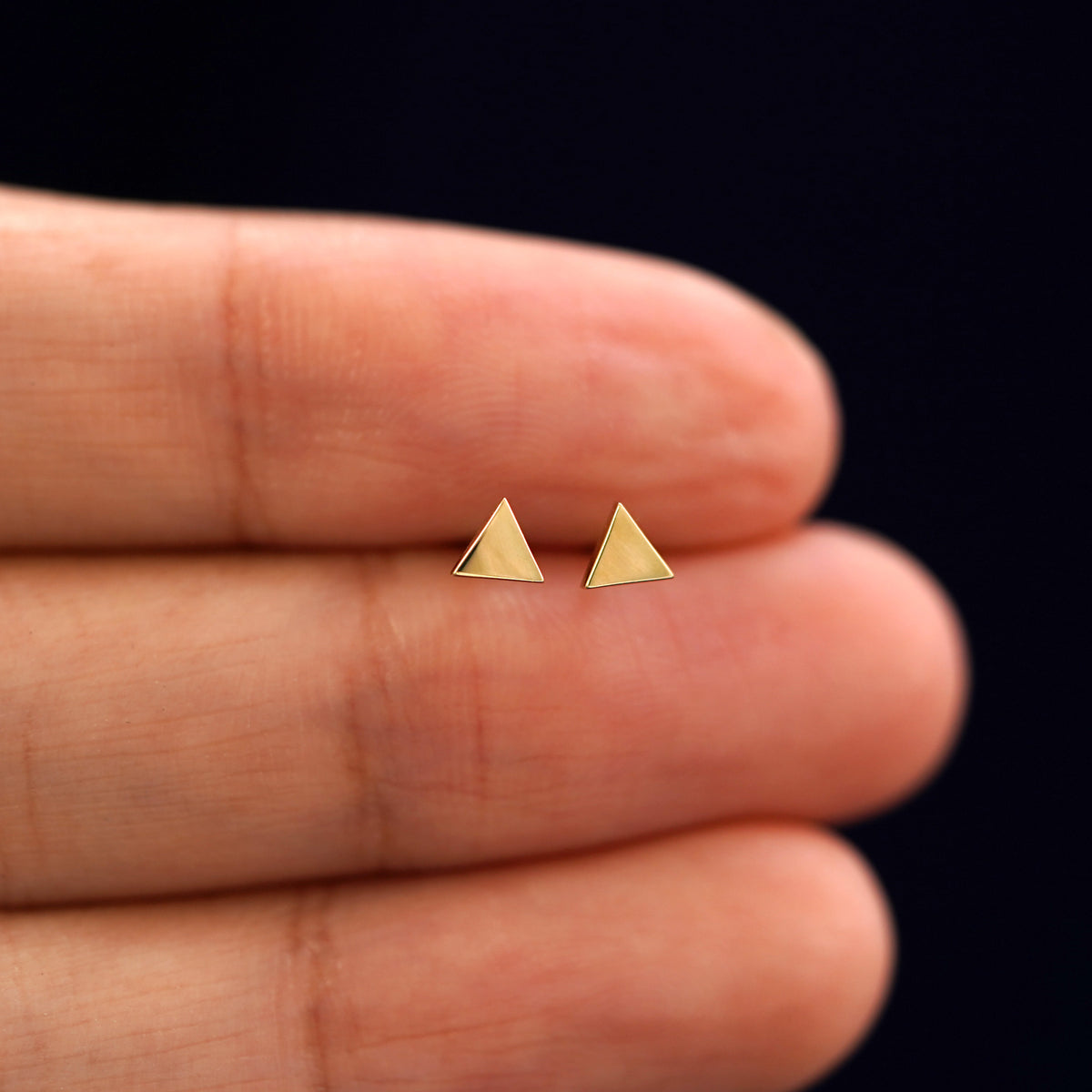 A model's hand holding a pair of recycled 14k gold Triangle Earrings