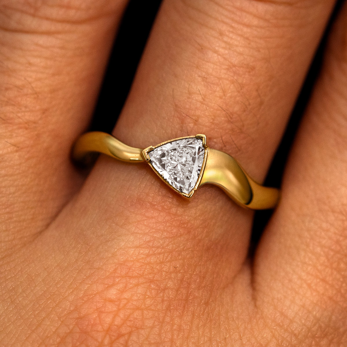 A model's hand wearing a 14k yellow gold Trillion Lab Clear Diamond Wavy Ring