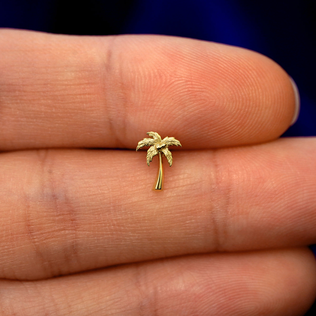 A model holding a solid gold Palm Tree stud earring between two fingers