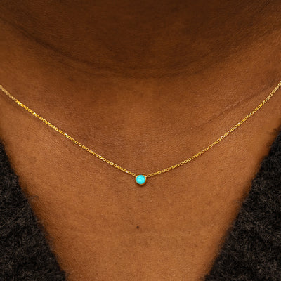Close up view of a model neck wearing a 14k yellow gold Bezel set Turquoise gemstone necklace 
