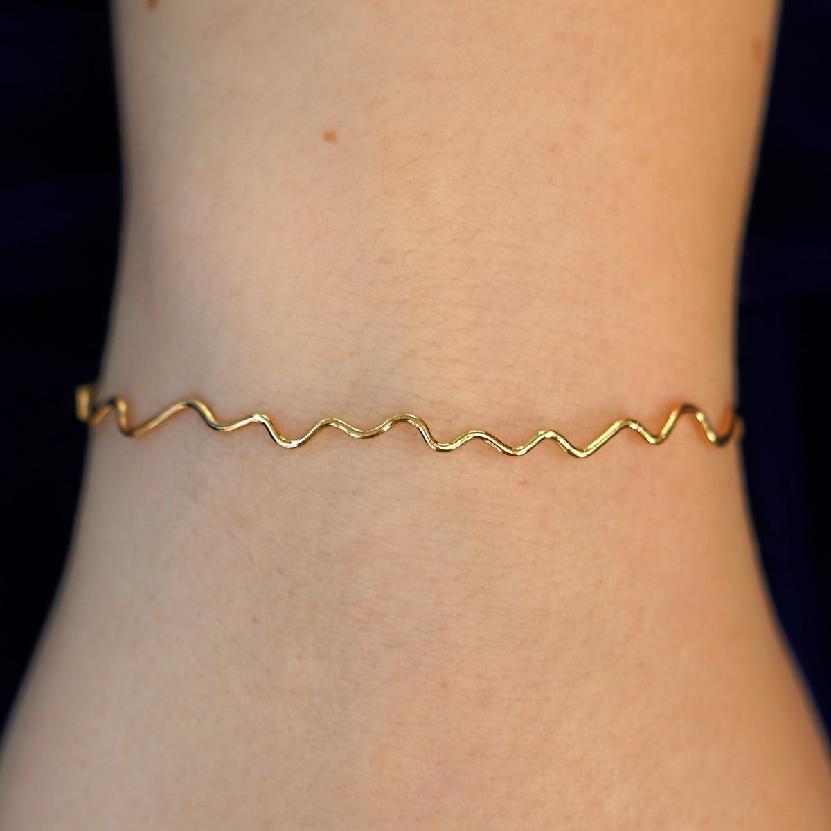 A model's wrist wearing a 14k gold Wave Bangle Bracelet