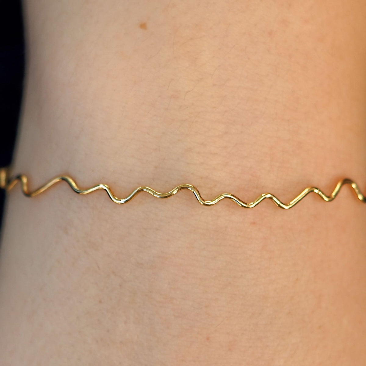 Close up view of a model's wrist wearing a 14k gold Wave Bangle Bracelet