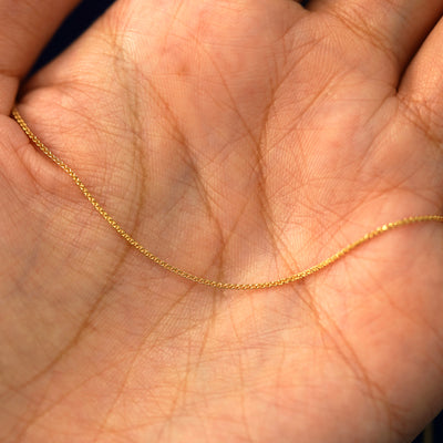 A yellow gold Wheat Chain draped on a model's palm