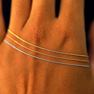 Close up view of a model's wrist wearing three versions of the Wheat Necklace in yellow, rose, and white gold