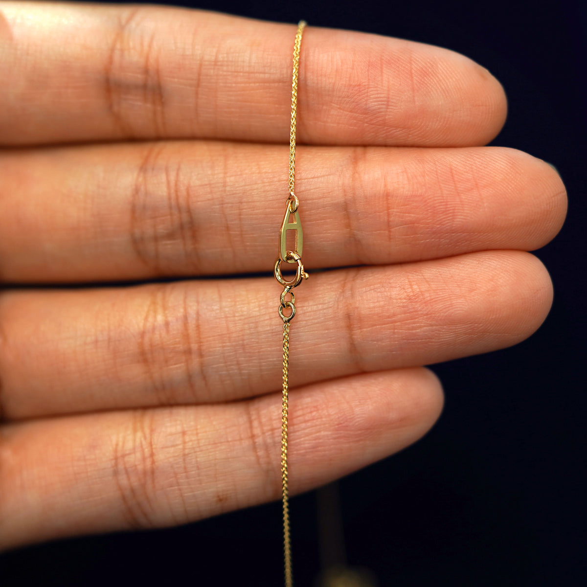 A model's hand holding an Automic Gold AU spring ring lock on a yellow gold Wheat Chain