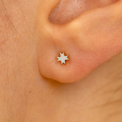 Close up view of a model's ear wearing a white gold 8 pointed star earring
