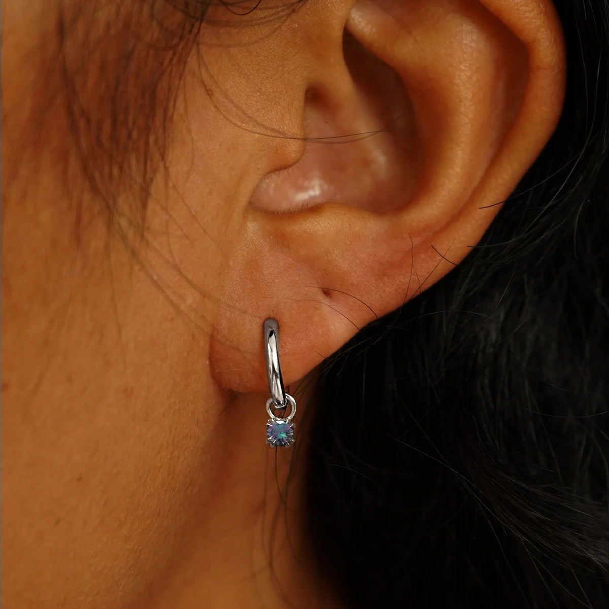 Close up view of a model's ear wearing a white gold Alexandrite Charm on a Curvy Huggie Hoop