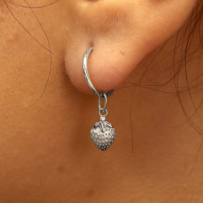 Close up view of a model's ear wearing a white gold Strawberry Charm on a Small Seamless Huggie Hoop
