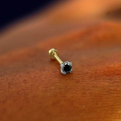 A solid 14k white gold Black Diamond Flatback Piercing resting on the back of a model's hand