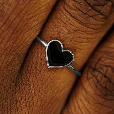 Close up view of a model's fingers wearing a 14k white gold black enamel heart ring