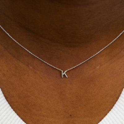 Close up view of a model's neck wearing a 14k solid white gold Block Initial Necklace in the letter K