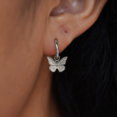 Close up view of a model's ear wearing a white gold Butterfly Charm on a Curvy Huggie Hoop