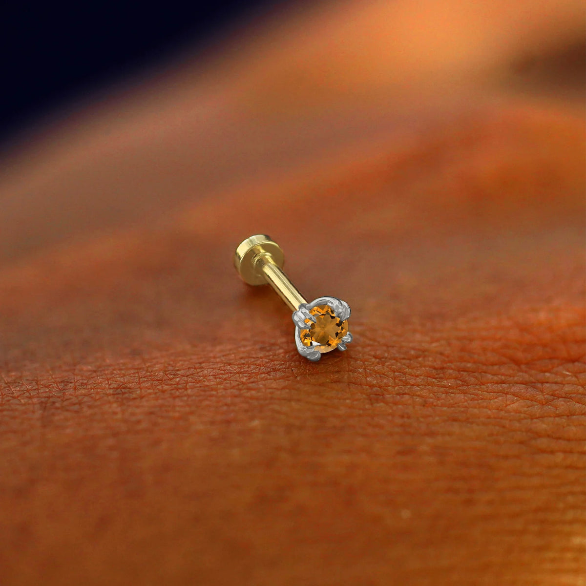 A solid 14k white gold Citrine Flatback Piercing resting on the back of a model's hand