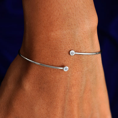 Close up view of a model's wrist wearing a 14k white gold clear diamond gemstone bypass bangle