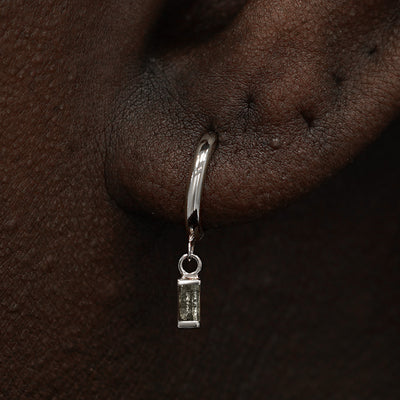 Close up view of a model's ear wearing a white gold Baguette Diamond Dangle Huggie Hoop