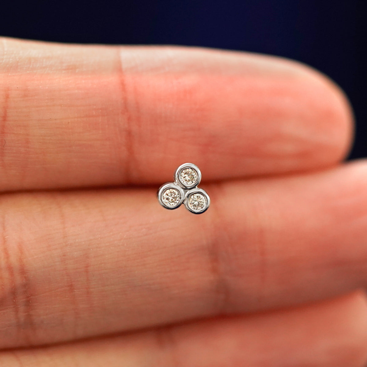 A hand holding a 14k white gold Diamond Trio stud earring in between their fingers