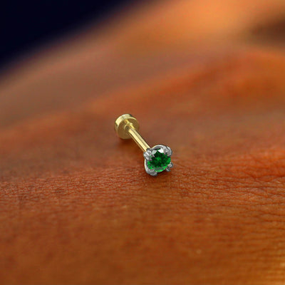 A solid 14k white gold emerald Flatback Piercing resting on the back of a model's hand