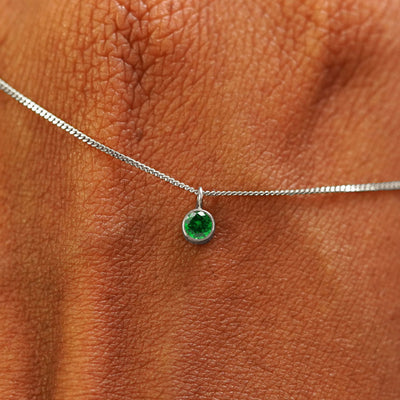 Close up view of a 14k white gold Emerald Necklace draped across the back of a model's hand