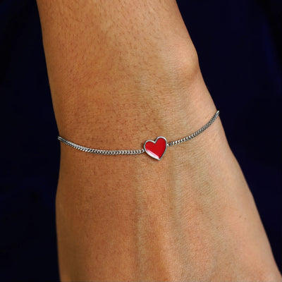 Close up view of a model's wrist wearing a white gold red enamel heart bracelet