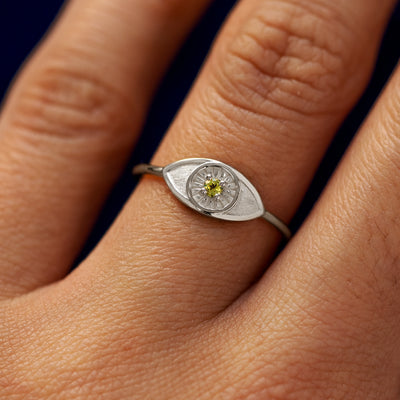 Close up view of a model's hand wearing a white gold Evil Eye Ring in the Emerald gemstone option