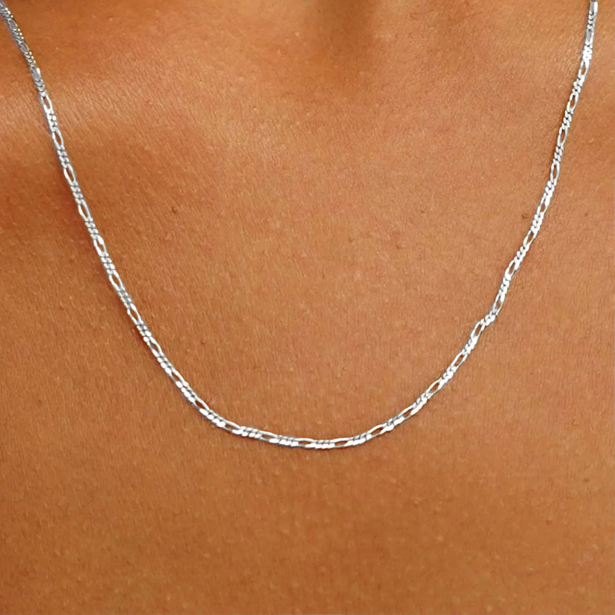 Close up view of a model's neck wearing a solid white gold Figaro Chain