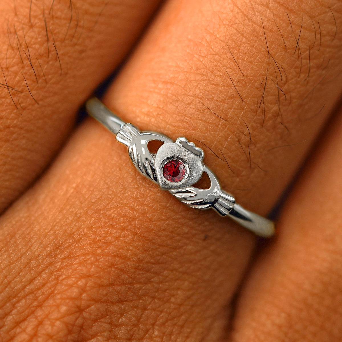 Close up view of a model's fingers wearing a 14k white gold ruby Thin Gemstone Claddagh Ring