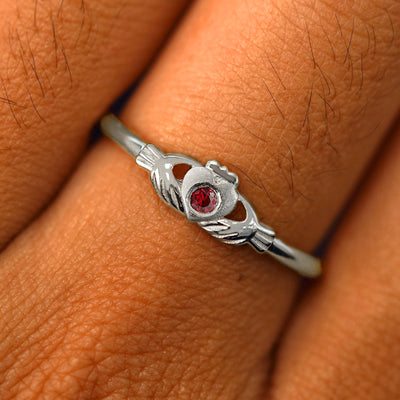 Close up view of a model's fingers wearing a 14k white gold ruby Thin Gemstone Claddagh Ring