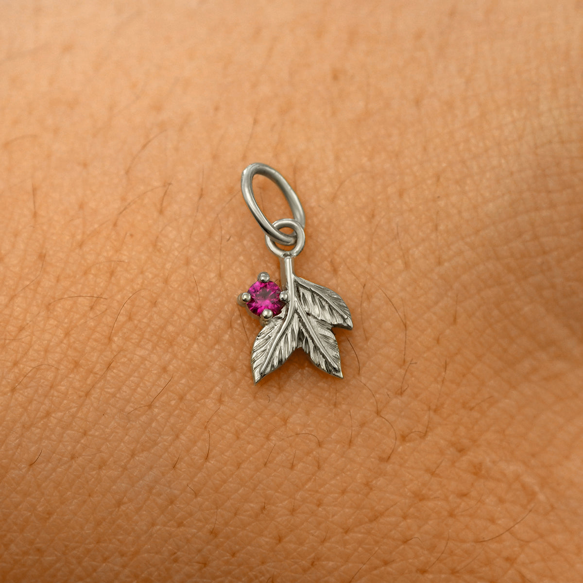 A solid 14k white gold ruby Gemstone 3 Leaves Charm resting on the back of a model's hand