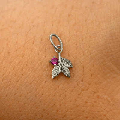 A solid 14k white gold ruby Gemstone 3 Leaves Charm resting on the back of a model's hand