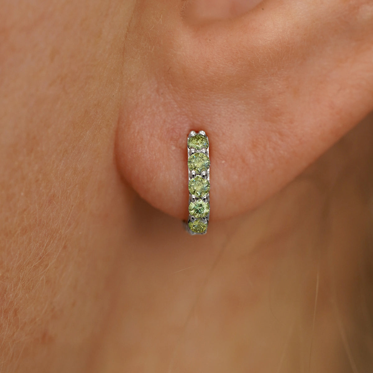 Close up view of a model's ear wearing a white gold Mini Light Green Lab Diamond Huggie Hoop